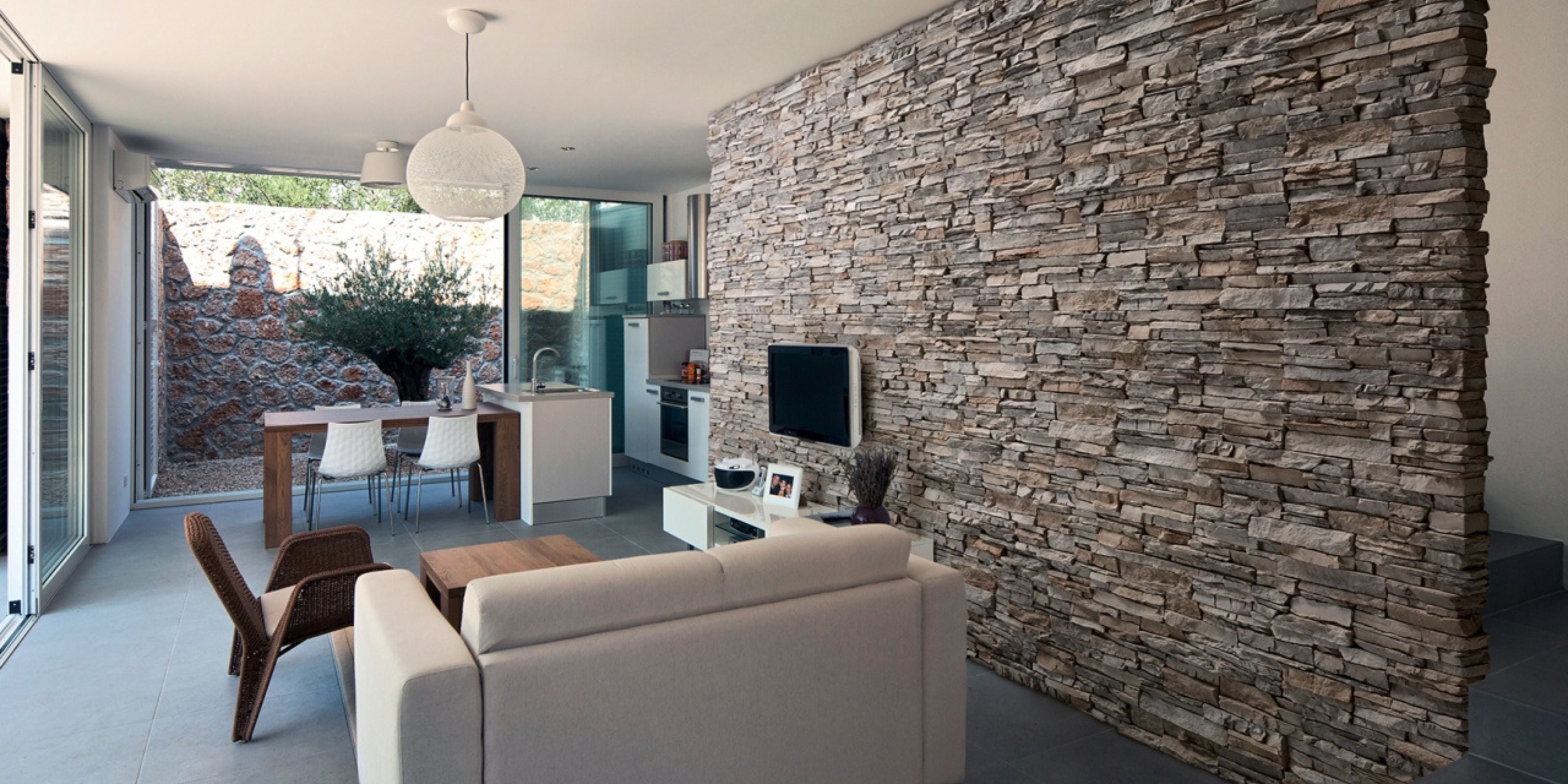 Modern open-plan living room and kitchen featuring a striking stonework cladding accent wall with split-face stone texture, highlighting contemporary interior design using natural materials