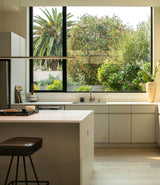 Modern minimalist kitchen with light cabinets, a white island, gas stove, and large window overlooking greenery